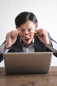 Zdziwiona osoba spogląda przez okulary na ekran laptopa